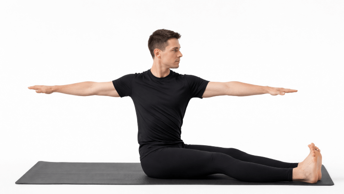 ピラティスのスパインローテーションのポーズをする男性